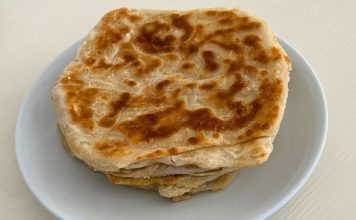 Katmer Pişirme: Geleneksel Hamurun Sofralardaki Yeri Katmer, özellikle Anadolu ve Güneydoğu mutfaklarının vazgeçilmez hamur tatlarından biridir. İnce açılan hamurun kat kat yoğrulup pişirilmesiyle elde edilen bu lezzet, hem kahvaltı sofralarının hem de çay saatlerinin olmazsa olmazlarından biridir. Katmer, fırınlama veya sacda pişirme teknikleriyle hazırlanabilir, her yöntemde kendine özgü dokusunu ve lezzetini korur. Konulu bir haber görseli.