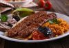 Kebap, Türk mutfağının en köklü ve en tanınan lezzetlerinden biri olarak, yalnızca bir yemek değil aynı zamanda bir yaşam biçimi olarak da değerlendirilebilir. Etin ateşle buluştuğu bu eşsiz teknik, binlerce yıllık geçmişe sahiptir ve tarih boyunca birçok uygarlığın mutfağında kendine yer bulmuştur. Ancak Anadolu toprakları, kebap kültürünü sadece korumakla kalmamış, aynı zamanda onu çeşitlendirip zenginleştirmiştir. Konulu bir haber görseli.
