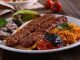 Kebap, Türk mutfağının en köklü ve en tanınan lezzetlerinden biri olarak, yalnızca bir yemek değil aynı zamanda bir yaşam biçimi olarak da değerlendirilebilir. Etin ateşle buluştuğu bu eşsiz teknik, binlerce yıllık geçmişe sahiptir ve tarih boyunca birçok uygarlığın mutfağında kendine yer bulmuştur. Ancak Anadolu toprakları, kebap kültürünü sadece korumakla kalmamış, aynı zamanda onu çeşitlendirip zenginleştirmiştir. Konulu bir haber görseli.
