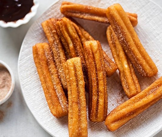 Churros, İspanya kökenli, kızartılarak hazırlanan tatlı hamur çubuklarıdır. 19. yüzyılda İspanya’da ortaya çıkan bu lezzet, kısa sürede Latin Amerika ve dünyanın farklı bölgelerine yayılmıştır. Geleneksel olarak kahvaltıda veya akşamüstü çay saatlerinde tüketilen churros, sıcak çikolata veya karamel sosla birlikte sunulur. Konulu bir haber görseli.