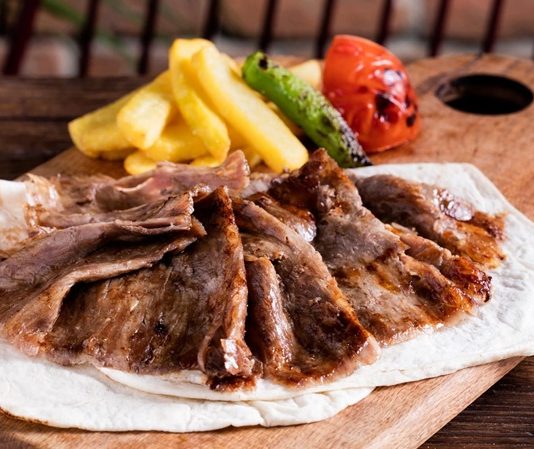 Türk mutfağının en önemli lezzetlerinden biri olan et döner, tarihsel olarak Osmanlı döneminden günümüze kadar uzanan bir yolculuğa sahiptir. Yatay şişlerde pişirilen etlerin zamanla dikey şişlere geçirilmesiyle ortaya çıkan bu yöntem, özellikle hızlı servis imkânı ve eşsiz lezzetiyle kısa sürede halkın gözdesi haline gelmiştir. Dönerin geçmişi, yalnızca bir yemeğin tarihi değil, aynı zamanda Anadolu’nun kültürel çeşitliliğinin de bir yansımasıdır. Konulu bir haber görseli.
