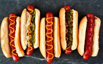 Hot Dog: Sokak Lezzetlerinin Vazgeçilmezi Dünya mutfağında geniş bir yer edinen hot dog, özellikle Amerika Birleşik Devletleri’nde adeta bir sembol haline gelmiştir. Kökeni 19. yüzyılın sonlarına kadar uzanan bu yiyecek, Almanya’dan Amerika’ya göç edenlerin beraberinde getirdiği sosis kültürü ile ortaya çıkmıştır. Uzun ekmek arasına yerleştirilen sosisin seneler içinde farklı soslarla buluşması, hot dog’u bugünkü popüler formuna kavuşturmuştur. Konulu bir haber görseli.