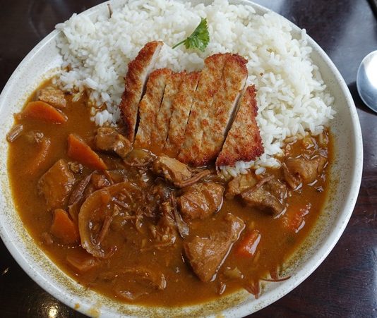 Katsu Curry, Japon mutfağının hem geleneksel hem de modern dokunuşlarını bir arada sunan özel bir yemektir. “Katsu” kelimesi çıtır kaplamalı kızarmış et kotletini ifade ederken, “curry” Japonya’ya 19. yüzyılda İngilizler aracılığıyla Hindistan’dan gelen köri baharat karışımını anlatır. Bu iki farklı unsurun birleşmesiyle ortaya çıkan yemek, Japonya’da kısa sürede popülerlik kazanmıştır. Konulu bir haber görseli.
