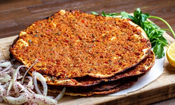 Türk mutfağının en sevilen lezzetlerinden biri olan lahmacun, yüzyıllardır sofralarda kendine yer bulmaktadır. İnce açılmış hamurun üzerine kıyma, domates, soğan, maydanoz ve çeşitli baharatlarla hazırlanan iç harcın eklenmesiyle pişirilen bu eşsiz yemek, hem lezzeti hem de pratikliğiyle öne çıkar. Anadolu’nun farklı bölgelerinde yaygın olarak tüketilen lahmacun, özellikle Güneydoğu mutfağının vazgeçilmezleri arasında yer almaktadır. Konulu bir haber görseli.