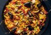 Paella, İspanya’nın en bilinen yemeklerinden biri olarak dünya mutfağında önemli bir yere sahiptir. Özellikle Valencia bölgesinde ortaya çıkan bu yemek, zamanla tüm ülkeye ve oradan da dünyaya yayılmıştır. Tarihi 15. yüzyıla kadar uzanan paella, köylülerin tarlalarda buldukları malzemeleri bir araya getirerek pişirdikleri pratik bir yemek olarak doğmuştur. Konulu bir haber görseli.