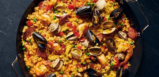 Paella, İspanya’nın en bilinen yemeklerinden biri olarak dünya mutfağında önemli bir yere sahiptir. Özellikle Valencia bölgesinde ortaya çıkan bu yemek, zamanla tüm ülkeye ve oradan da dünyaya yayılmıştır. Tarihi 15. yüzyıla kadar uzanan paella, köylülerin tarlalarda buldukları malzemeleri bir araya getirerek pişirdikleri pratik bir yemek olarak doğmuştur. Konulu bir haber görseli.