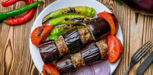 Türk mutfağının vazgeçilmez lezzetlerinden biri olan patlıcan kebabı, özellikle Gaziantep, Şanlıurfa ve Adana gibi şehirlerde sıkça hazırlanır. Patlıcanın közlenip etle buluşmasıyla ortaya çıkan bu yemek, hem hafif hem de doyurucu bir öğün sunar. Osmanlı mutfağından günümüze uzanan tarif, yöresel farklılıklarla her sofrada kendine özgü bir tat bırakır. Konulu bir haber görseli.