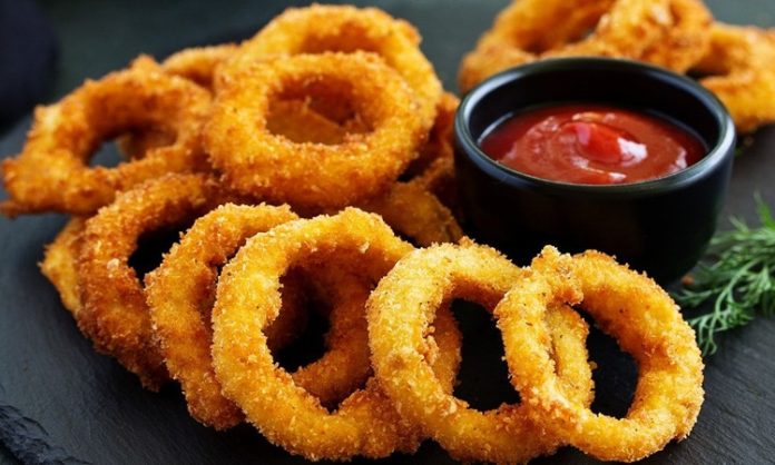 Soğan halkası, fast food kültürünün en sevilen atıştırmalıklarından biri olarak öne çıkıyor. Tarihi 20. yüzyılın ortalarına dayanan bu lezzet, özellikle Amerika’da popülerlik kazanmış ve kısa sürede dünya mutfaklarına yayılmıştır. Patates kızartmaları ve burgerlerin yanında ikincil lezzet olarak sunulan soğan halkaları, hem çıtır dokusu hem de tatlımsı soğan aroması ile dikkat çekiyor. Konulu bir haber görseli.