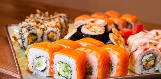 Sushi Roll: Dünyada Popülerliği Artan Japon Lezzeti Sushi roll, Japon mutfağının en bilinen yemeklerinden biridir ve dünya genelinde ün kazanmıştır. İlk olarak Edo döneminde ortaya çıkan sushi, başlangıçta balığın pirinç içinde fermente edilmesiyle hazırlanıyordu. Zaman içinde bu yöntem değişti ve daha modern bir hale geldi. Özellikle 20. yüzyılın ortalarında Amerika’da popülerleşen sushi roll, farklı malzemelerin bir araya gelmesiyle çeşitlenerek bugünkü halini aldı. Konulu bir haber görseli.