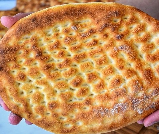 Türk mutfağının en sevilen ekmek çeşitlerinden biri olan tırnak pide, özellikle Ramazan sofralarının ve kebapçıların vazgeçilmez lezzetleri arasında yer alır. Yumuşak içi ve hafif çıtır kabuğu ile öne çıkan bu pide, hem sade olarak hem de farklı yemeklerin eşlikçisi şeklinde tüketilir. Tırnak pide, adını hamura parmak uçlarıyla yapılan tırnak izlerinden alır ve bu izler pişirme sırasında pideye özgün bir görünüm kazandırır. Hem görselliği hem de tadıyla sofraları süsleyen bu geleneksel lezzet, Anadolu’nun mutfak kültüründe önemli bir yere sahiptir. Konulu bir haber görseli.